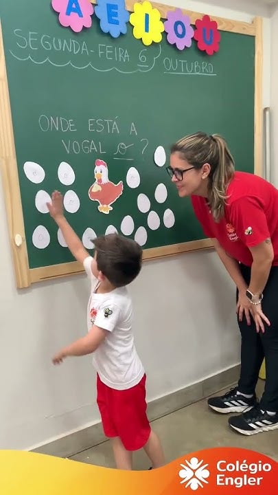 Professora e aluno na atividade das vogais, no quadro da sala de aula